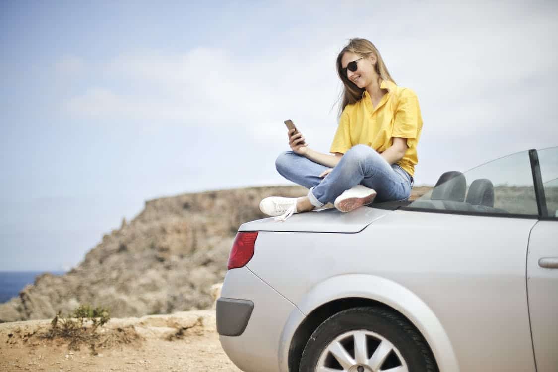 Foto Mujer en blusa amarilla y pantalones vaqueros azules tomando Selfie sentado en el coche de stock gratuita