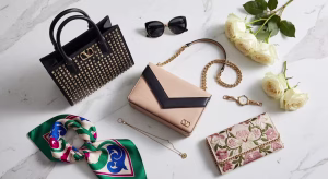 Composición flat lay de tres bolsos icónicos Valentino Garavani sobre mármol: Rockstud negro, VSLING beige y clutch DeVain bordado con accesorios de lujo