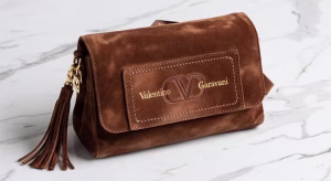 Guía completa de bolsos Valentino Garavani: los modelos imprescindibles que definen el lujo contemporáneo Detalle del bolso Valentino Garavani Nellcôte en ante marrón mostrando textura bohemia y artesanía italiana sobre superficie de mármol