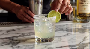 Margarita premium con borde de sal y lima fresca servida en vaso de cóctel sobre barra de mármol